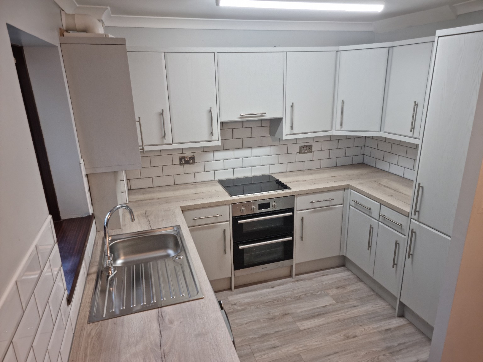 Finished U-shaped kitchen with light grey framed doors, light wood-effect worktops and white tiles